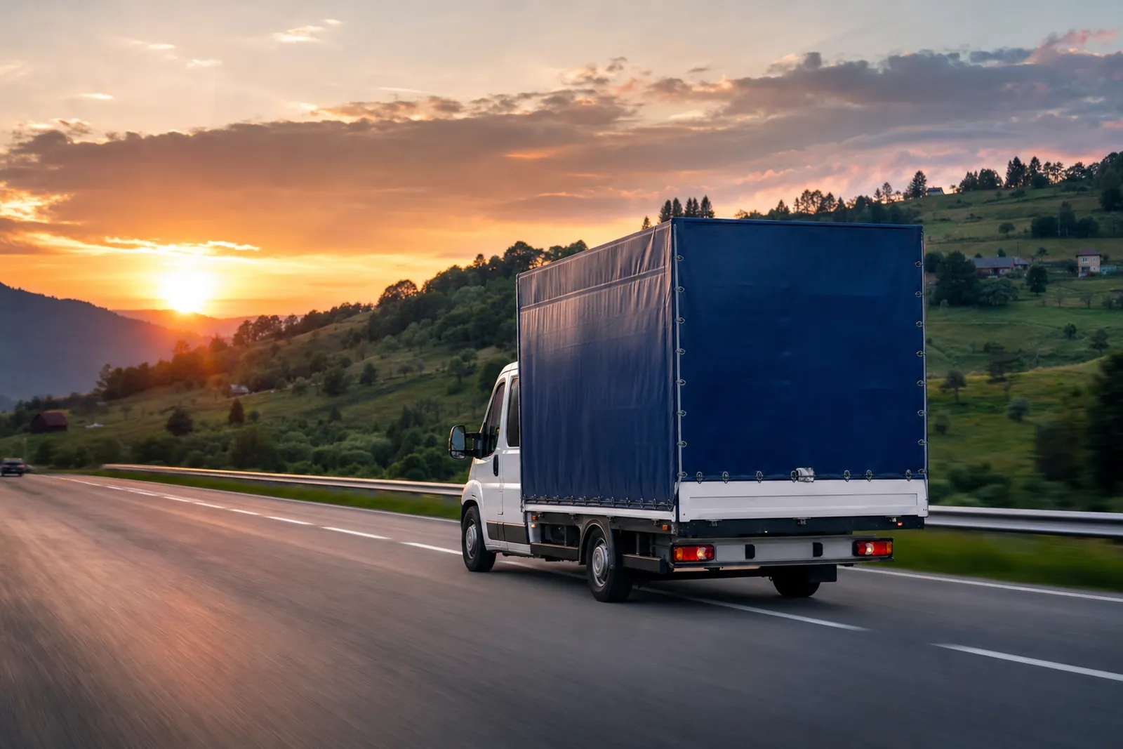 Dubă cu prelată pe autostradă, printre dealuri, la apus